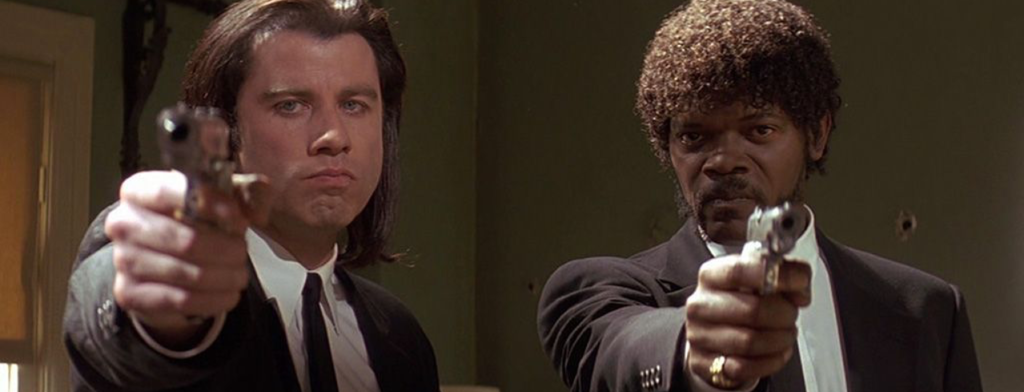 John Travolta and Samuel L. Jackson in black suits pointing at you with guns